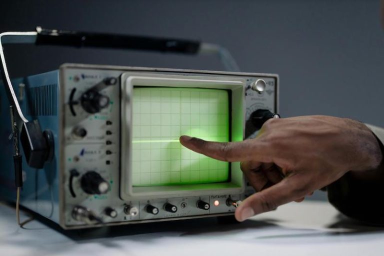 A person pointing to an oscilloscope.